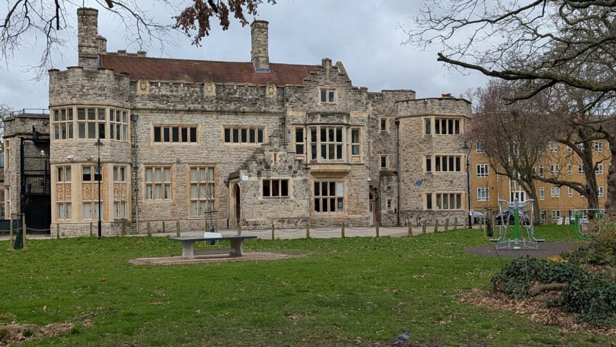 Stone Tudor-style building with a lawn and trees