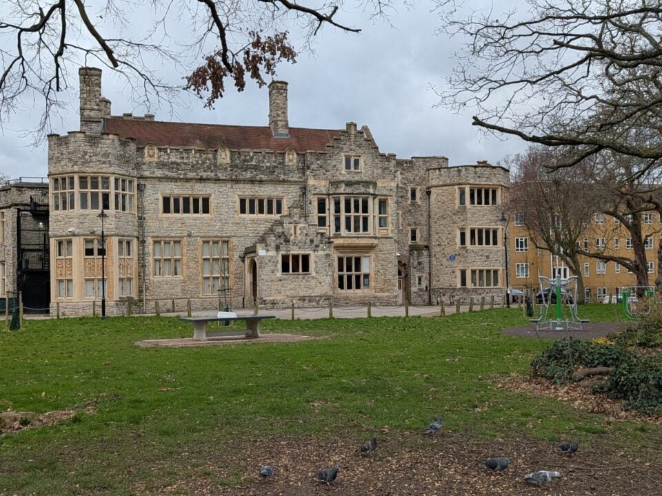 Stone Tudor-style building with a lawn and trees